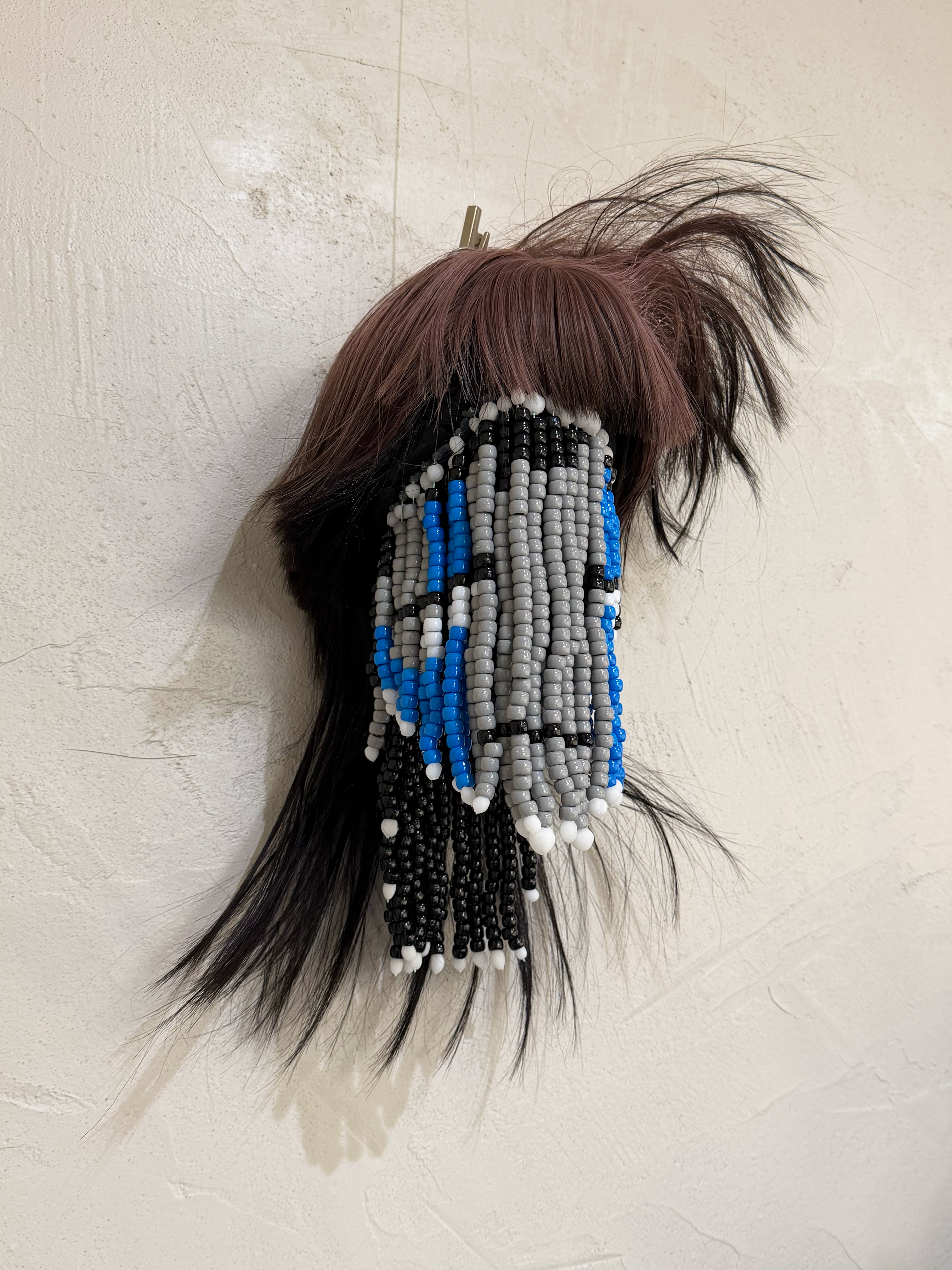 3/4 angle shot of a sculpture made using beads and a sythetic wig to represent a floating head.